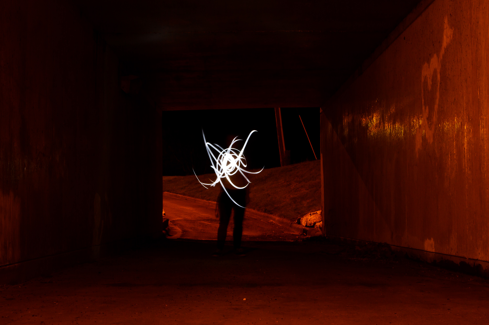 A subject stands at the end of a tunnel, but their head is covered by trails of white light in a scribble pattern