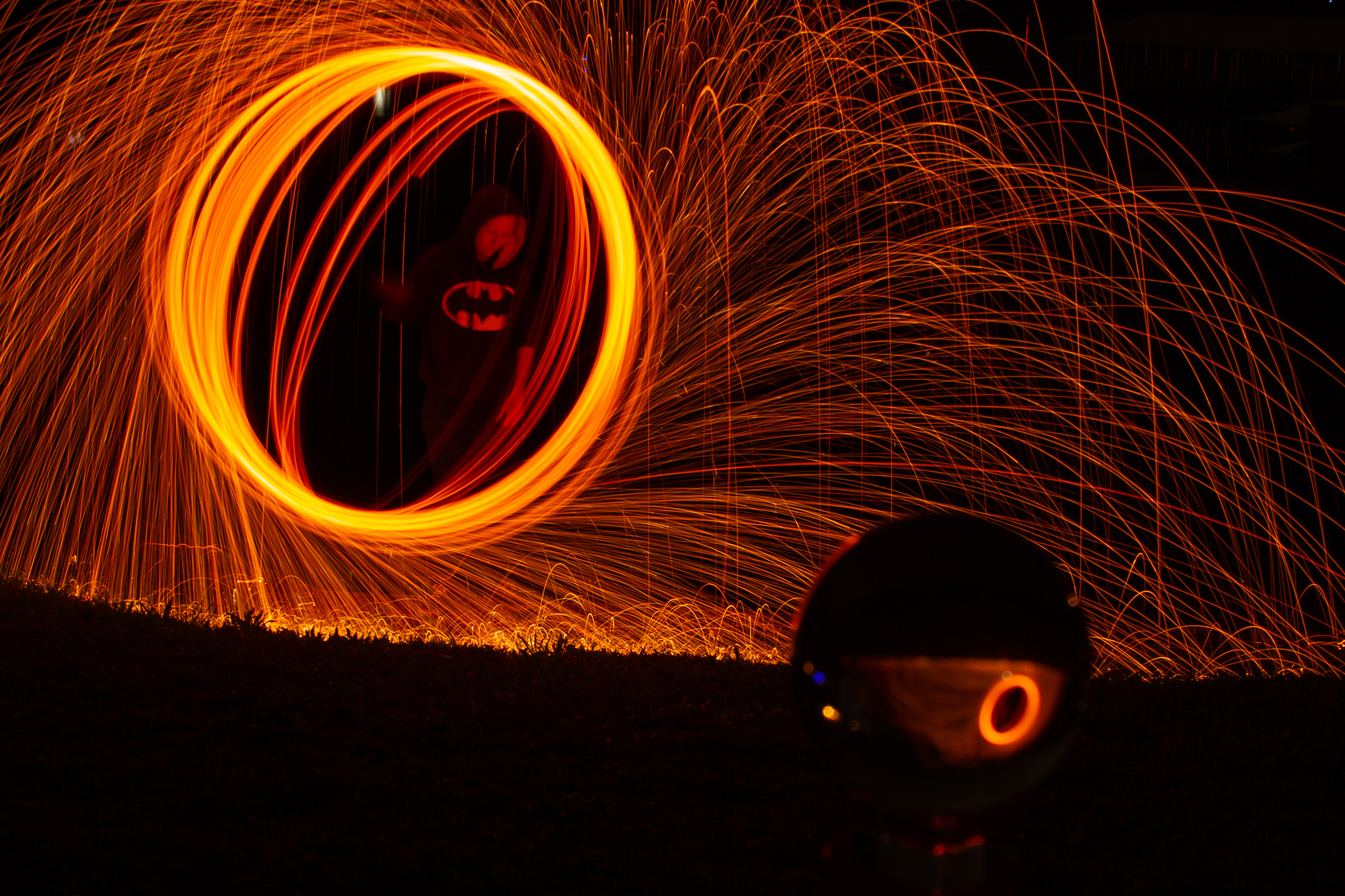 sparks fly in a circular motion around a subject wearing a batman hoodie, creating circular trails of light around them.