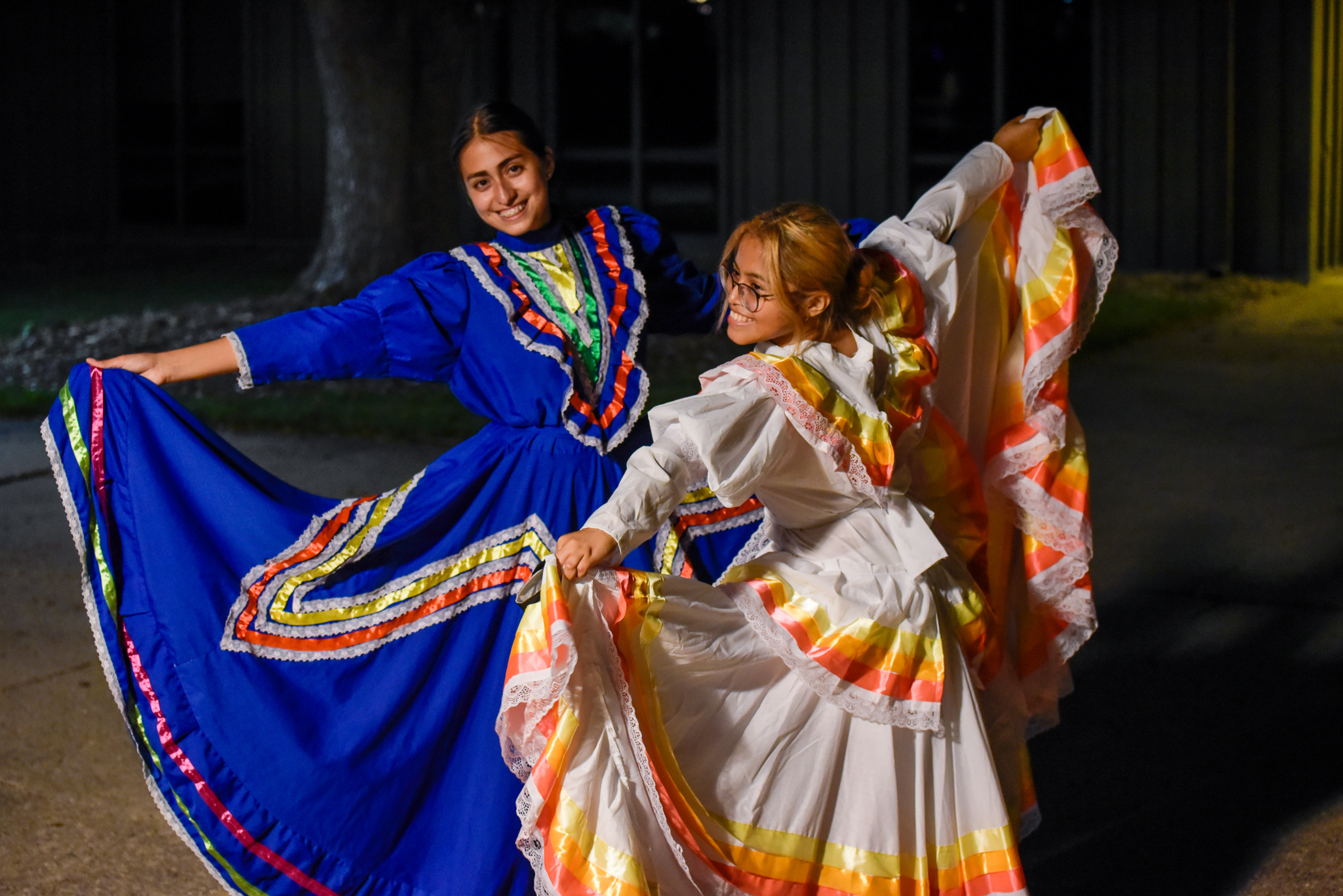 two girls in traditional mexican dresses smile and lift their dresses for a dance