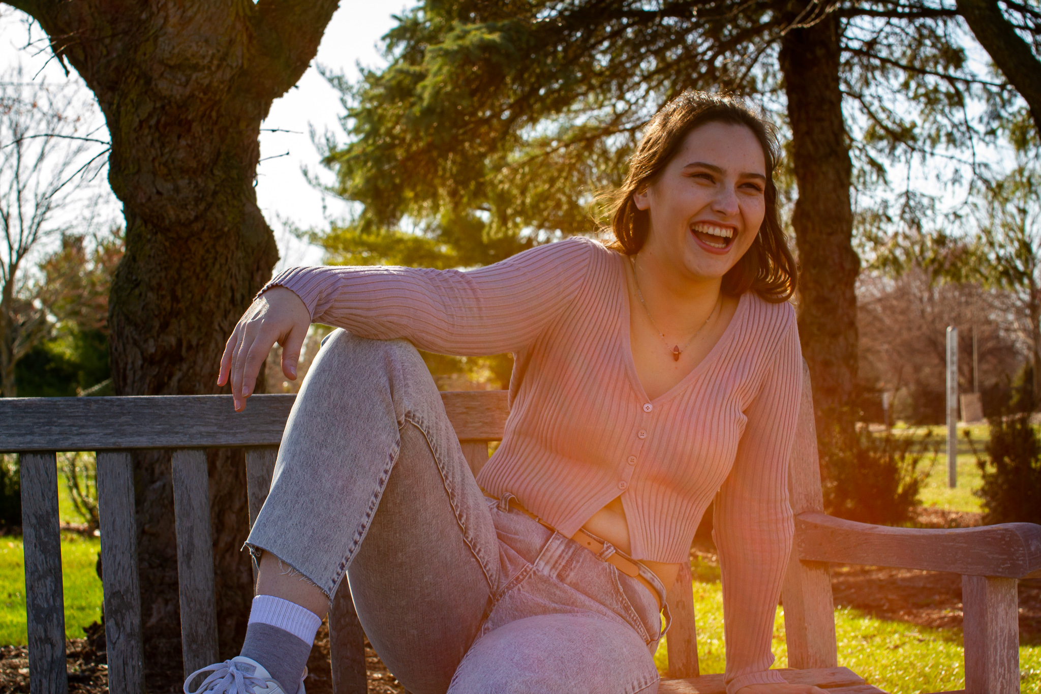 a young female sits on a park bench in a relaxed pose and looks away from the camera, smiling brightly and laughing