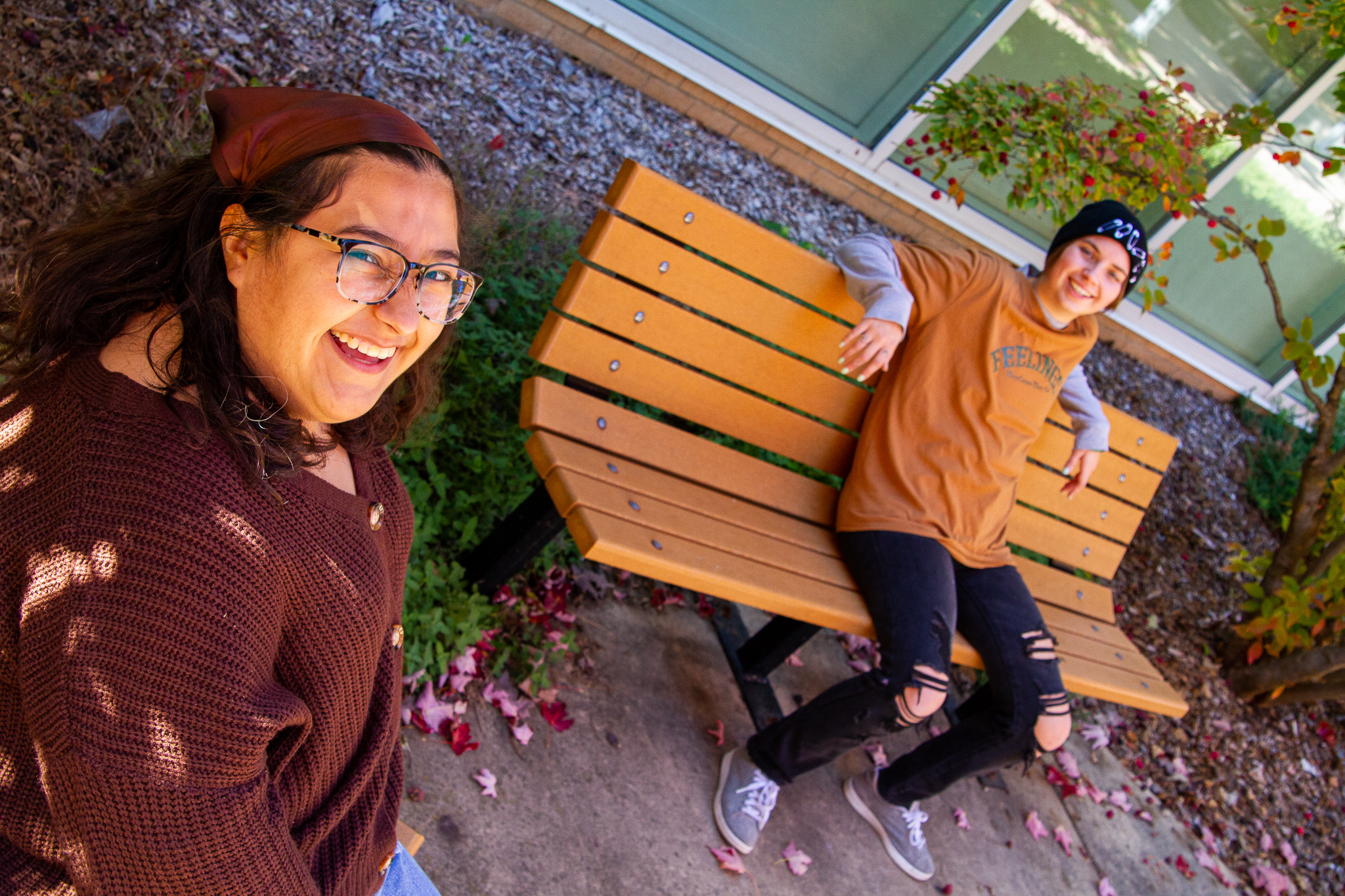 two young adults sit on seperate benches and glance up at the camera smiling for the photo